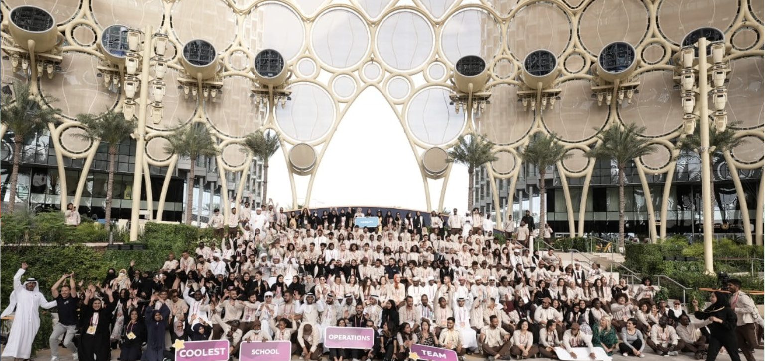 The Expo 2020 Dubai Al Wasl dome with a large group of school visitors gathered beneath it.